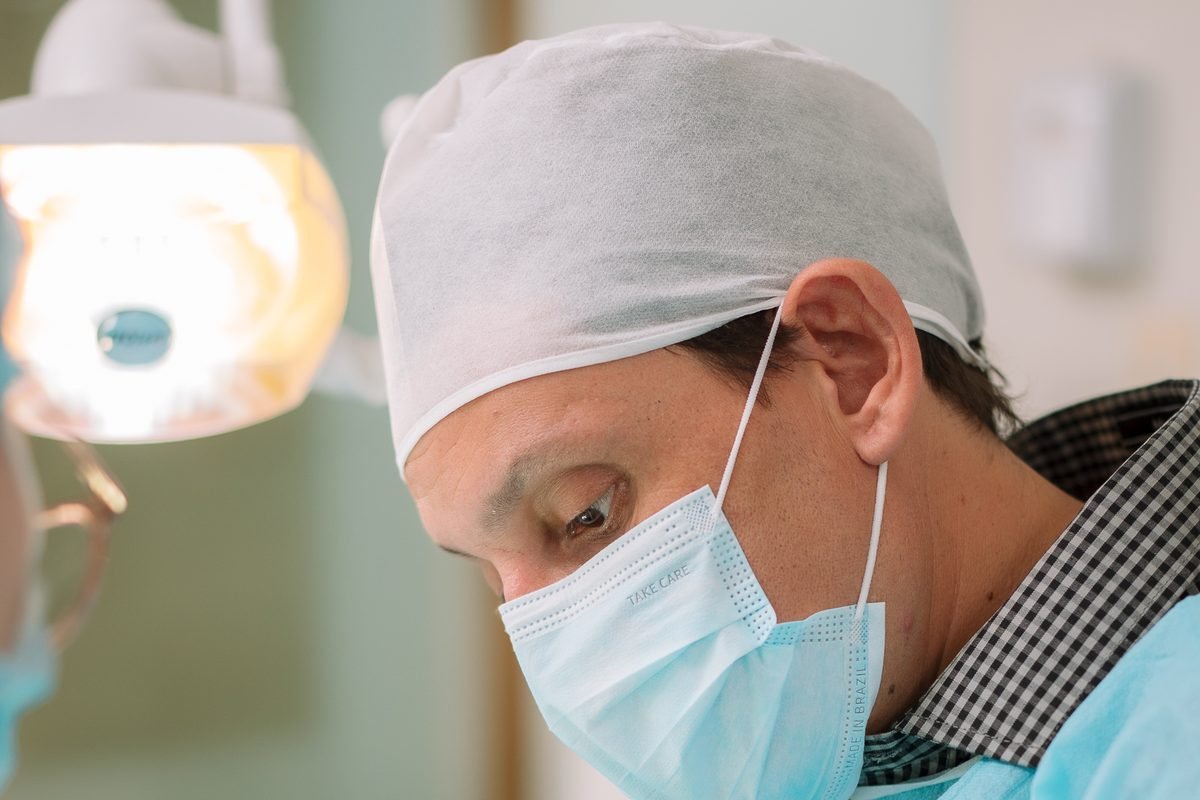 Dr. Reinaldo José Seco em atendimento clínico sob o refletor odontológico, no consultório da Zona 8, em Maringá.